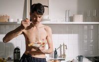 Young man enjoying a breakfast omelette in a sunlit kitchen setting.